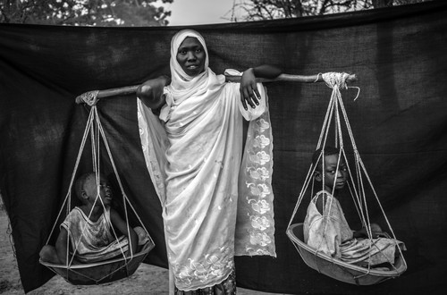 Several months before this picture was taken, repeated bombing raids forced Dowla, 22, and her six children to flee their village in Sudan’s Blue Nile state. The most important object she was able to bring with her is the wooden pole balanced over her shoulder, with which she carried her six children during the 10-day journey from Gabanit to South Sudan. At times, the children were too tired to walk, forcing her to carry two on either side. Doro refugee camp, Maban County, South Sudan.