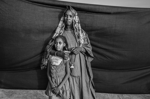 Malian refugee Hadeisha, 19, poses for a portrait with her niece (name unknown) near their shelter in Goudebou refugee camp, Burkina Faso, on 9 March, 2013. Hadeisha fled with her extended family when a strict version of Sharia law was imposed. Her husband stayed behind to tend their livestock. She still worries about him, as “he is in a very dangerous zone.” The most important object Hadeisha brought was a Tuareg necklace that belonged to her grandmother. She sometimes holds it, hoping it will bring a sort of spiritual protection to her husband. It also brings back memories of her childhood and happier times.